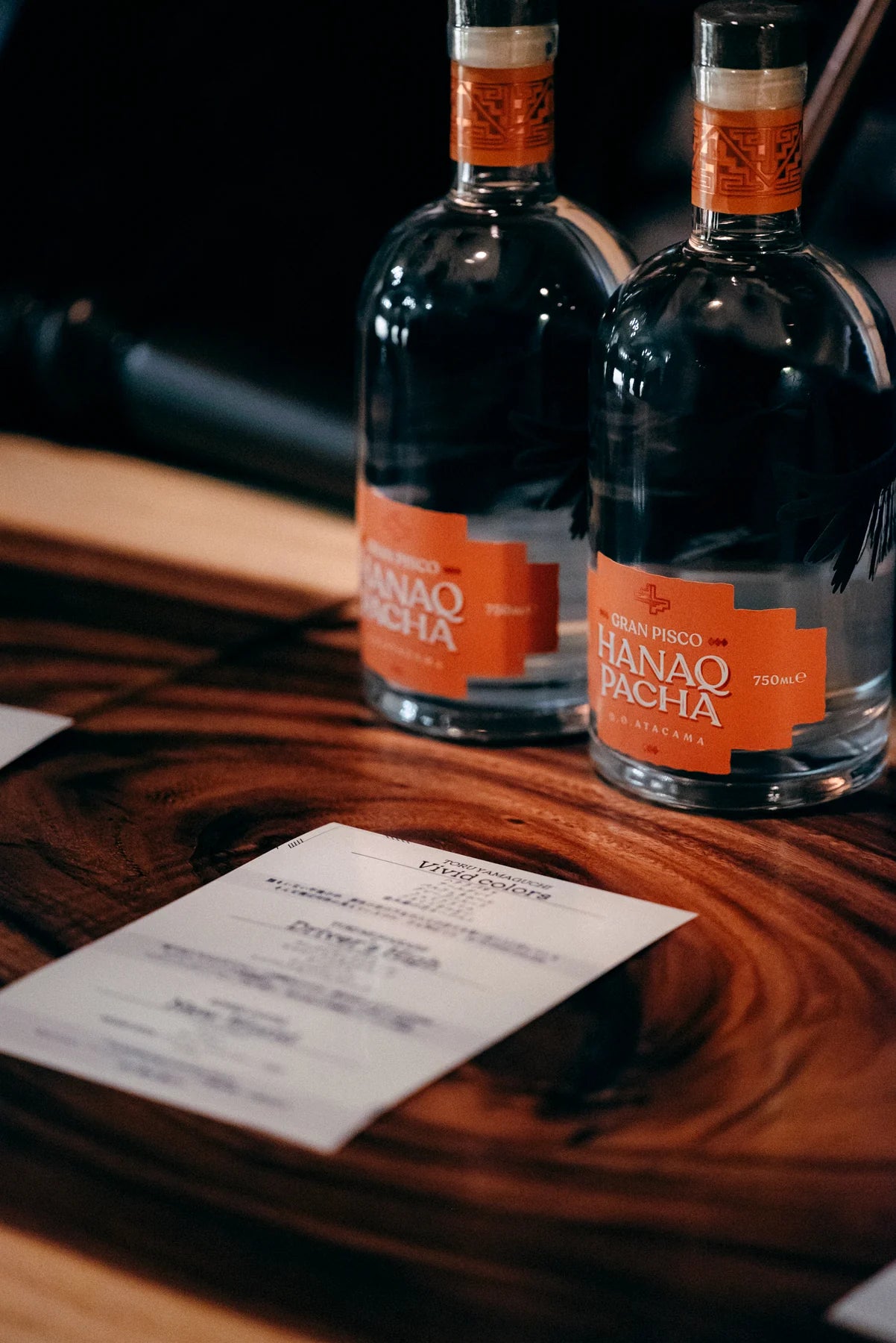 Botellas Hanaq Pacha sobre mesa de madera junto a menu de degustacion