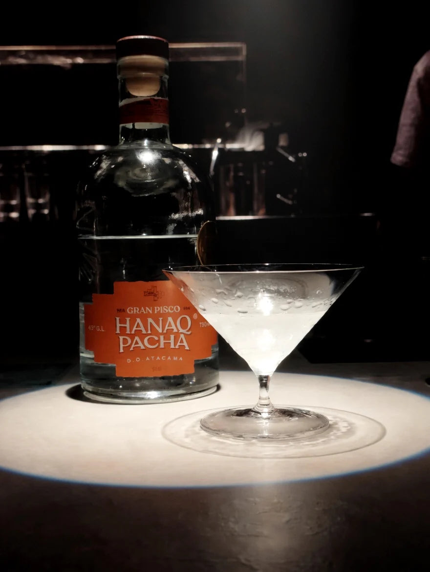 Botella Hanaq Pacha junto a copa coctel en barra oscura